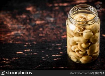 Pickled mushrooms in a glass jar on the table. Against a dark background. High quality photo. Pickled mushrooms in a glass jar on the table.