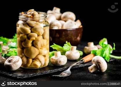 Pickled mushrooms in a jar with greens on a stone board. On a black background. High quality photo. Pickled mushrooms in a jar with greens on a stone board.