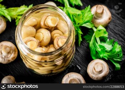 Pickled mushrooms in a jar with greens on a stone board. On a black background. High quality photo. Pickled mushrooms in a jar with greens on a stone board.