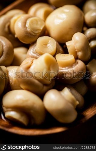 Pickled mushrooms in a wooden plate on the table. Against a dark background. High quality photo. Pickled mushrooms in a wooden plate on the table.