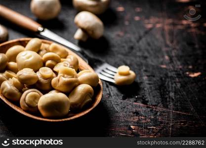 Pickled mushrooms in a wooden plate on the table. Against a dark background. High quality photo. Pickled mushrooms in a wooden plate on the table. 