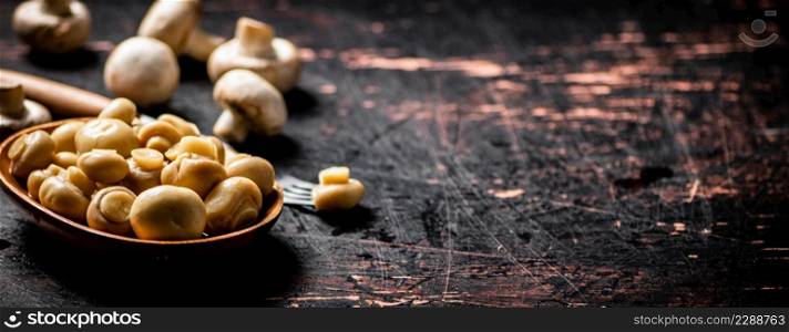 Pickled mushrooms in a wooden plate on the table. Against a dark background. High quality photo. Pickled mushrooms in a wooden plate on the table.