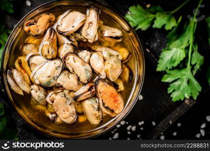 Pickled mussels in a bowl with parsley. On a black background. High quality photo. Pickled mussels in a bowl with parsley.