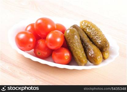pickled tomatoes and cucumbers on wooden table isolated on white