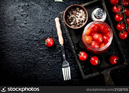 Pickled tomatoes in a glass jar on a cutting board. On a black background. High quality photo. Pickled tomatoes in a glass jar on a cutting board.