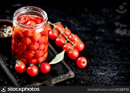 Pickled tomatoes in a glass jar on a cutting board. On a black background. High quality photo. Pickled tomatoes in a glass jar on a cutting board.