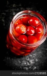 Pickled tomatoes in a glass jar on the table. On a black background. High quality photo. Pickled tomatoes in a glass jar on the table.