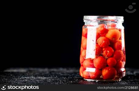 Pickled tomatoes in a glass jar on the table. On a black background. High quality photo. Pickled tomatoes in a glass jar on the table.