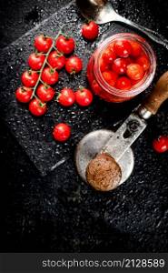 Pickled tomatoes in a jar on a stone board. On a black background. High quality photo. Pickled tomatoes in a jar on a stone board.