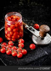 Pickled tomatoes in a jar on a stone board. On a black background. High quality photo. Pickled tomatoes in a jar on a stone board.