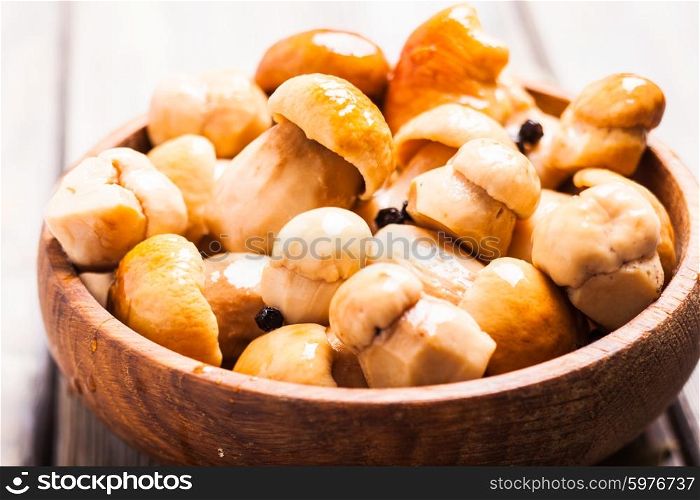 Pickled white boletus with black pepper and bay leaf in a wooden bowl. Pickled white boletus