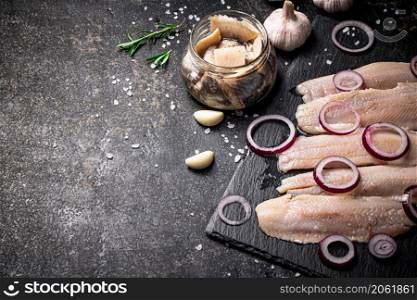Pickles of salted herring with onion rings. On a black background. High quality photo. Pickles of salted herring with onion rings.