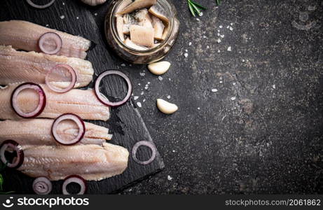 Pickles of salted herring with onion rings. On a black background. High quality photo. Pickles of salted herring with onion rings.