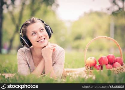 Picnic at summer park. Young attractive girl in summer park wearing headphones