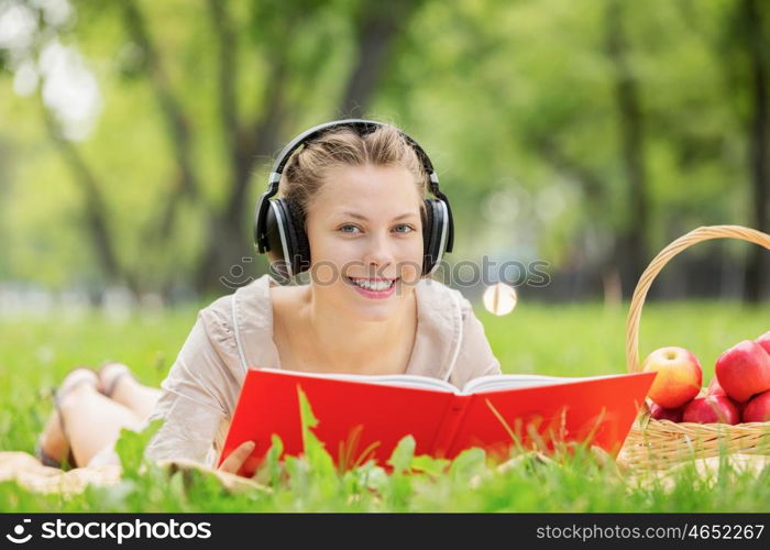 Picnic at summer park. Young attractive girl in summer park wearing headphones