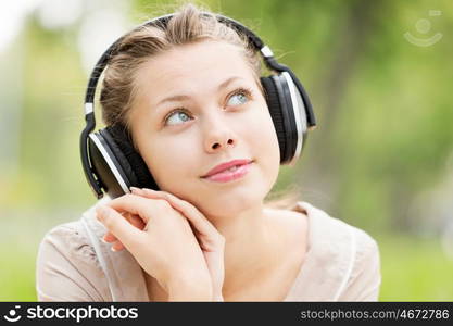 Picnic at summer park. Young attractive girl in summer park wearing headphones