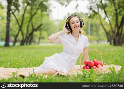 Picnic at summer park. Young attractive girl in summer park wearing headphones