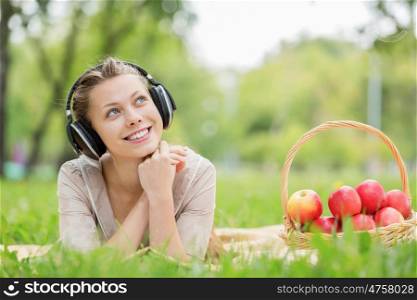 Picnic at summer park. Young attractive girl in summer park wearing headphones
