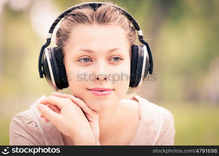 Picnic at summer park. Young attractive girl in summer park wearing headphones