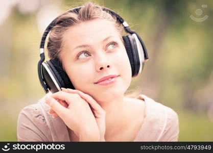 Picnic at summer park. Young attractive girl in summer park wearing headphones