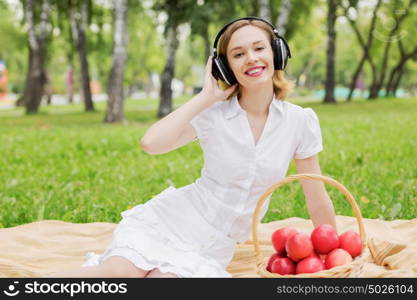 Picnic at summer park. Young attractive girl in summer park wearing headphones