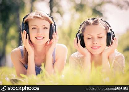 Picnic at summer park. Young attractive girls in summer park wearing headphones