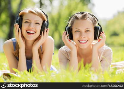 Picnic at summer park. Young attractive girls in summer park wearing headphones