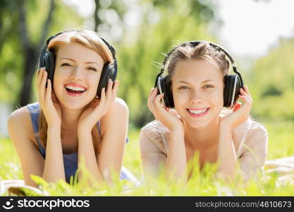 Picnic at summer park. Young attractive girls in summer park wearing headphones