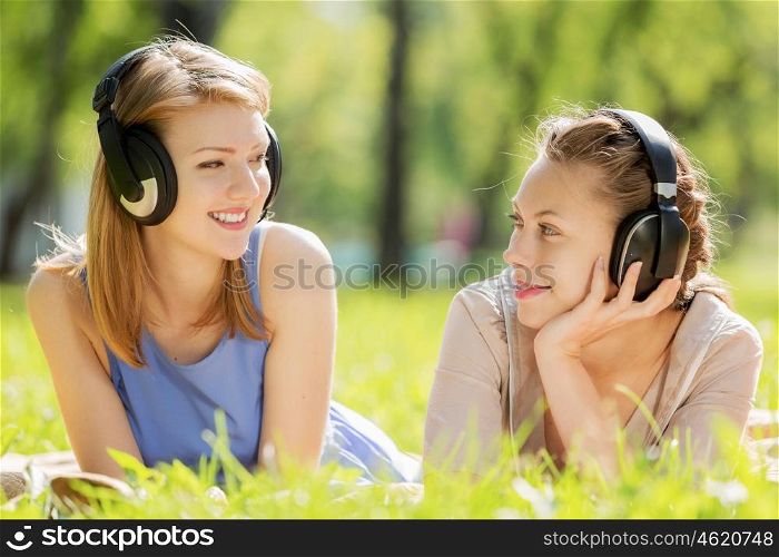 Picnic at summer park. Young attractive girls in summer park wearing headphones