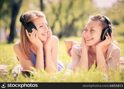 Picnic at summer park. Young attractive girls in summer park wearing headphones