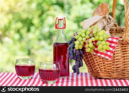 Picnic basket, grapes, juice and baguette on a red tablecloth. Sunny day. Picnic Concept. Picnic basket, grapes, juice and baguette on a red tablecloth