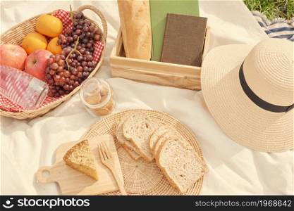 picnic concept picnic meal on the white cloth consisting of a basket of a water bottle, apples, oranges, and grapes, a loaf of bread, a jar of cookies and slices of bread.
