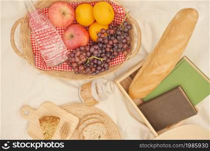 picnic concept picnic meal on the white cloth consisting of a basket of a water bottle, apples, oranges, and grapes, a loaf of bread, a jar of cookies and slices of bread.