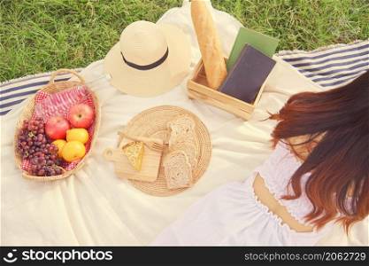 picnic concept The back of the maiden with long brown hair in the comfortable white dress lying down on the picnic cloth and reading a book.