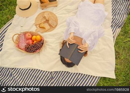 picnic concept The female in the gorgeous white dress sleeping on the white and blue striped cloth with the black book covering face while being on the nice picnic.