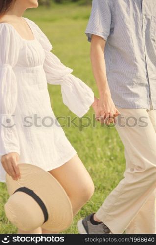 picnic concept The guy who wears bright blue top and beige pants taking the hand of the lady in white linin dress and walking on the grass field together.