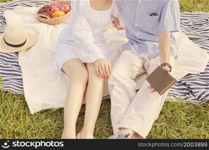 picnic concept The woman with white skirt and sandals sitting beside the man who puts on beige pants and grey sneakers.