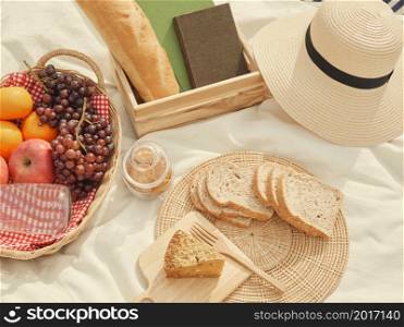 picnic concept There are a lot of things on the white cloth such as bread, fruits, a bottle of water, a hat and a notebook.