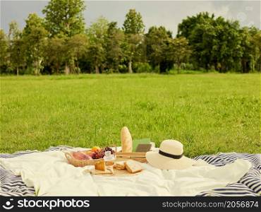 picnic concept There are a lot of things on the white cloth such as bread, fruits, a bottle of water, a hat and a notebook.