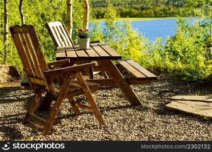 Picnic site rest stop area wooden chairs and table with flowers decoration on norwegian lake fjord shore. Holidays relaxation on trip. Scandinavia Europe.. Rest stop area picnic site on fjord lake shore