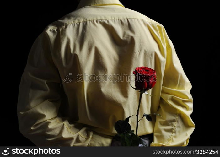 Picture a man in a yellow shirt holding a red rose behind his back.