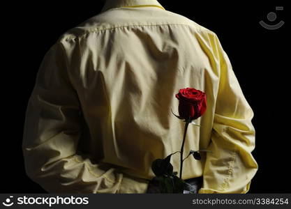 Picture a man in a yellow shirt holding a red rose behind his back.