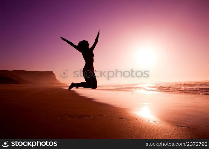 Picture of a female silhouette of a young girl jumping on the beach at the sunset