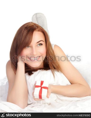 Picture of a happy young woman with gift box, cheerful female relaxing, laying down in the bed, isolated on white background, pretty girl portrait with romantic present, holiday celebrations concept