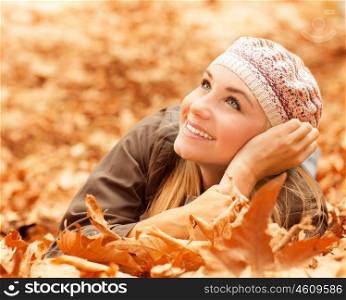 Picture of attractive female laying down on the ground covered dry autumnal foliage in beautiful park and looking up in sky, closeup portrait of pretty woman enjoying autumn weather in woods