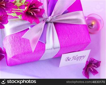 Picture of big pink present box, candle and purple flowers on the table at home, paper greeting card, happy mothers day, romantic holiday, gift for birthday, wedding day, romance and love concept