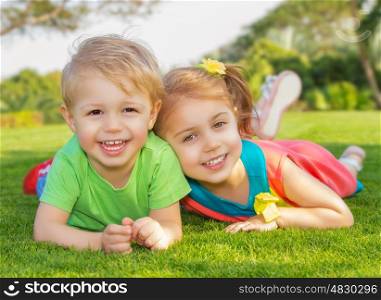 Picture of brother and sister having fun in the park, two cheerful child laying down on green grass, little girl and boy playing outdoors, best friends, happy family, love and happiness concept