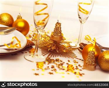 Picture of Christmas romantic table setting, two glasses for champagne adorned with golden ribbon, beautiful little candle, gold shiny bauble, holiday dinner in restaurant, New Year party
