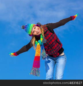 Picture of cute cheerful girl enjoying winter holidays, pretty young lady playing outdoors in winter cold weather, smiling woman with raised up hands isolated on blue sky background, Christmas holiday
