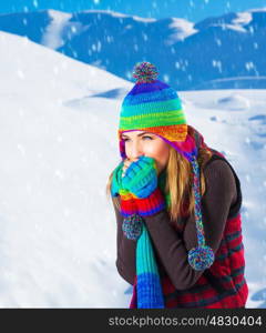 Picture of cute female in winter mountains, snowfall outdoors, beautiful woman wearing colorful wool hat, scarf and gloves, woman froze outdoor in cold snowy weather, wintertime holidays